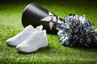 Rebel white cheer shoes on turf field next to pom pom and megaphone