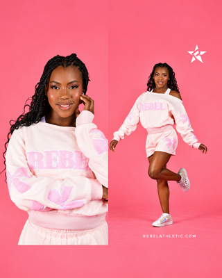 A model wearing a light pink Rebel Athletics sweatshirt and matching shorts set against a solid pink background, shown in both a close-up and full-body pose.