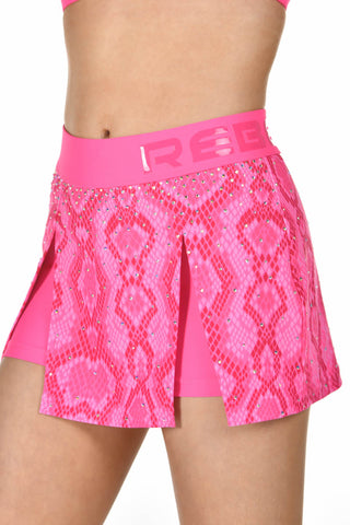 A close-up of a model wearing a bright pink athletic skirt with a snakeskin pattern and a wide elastic waistband featuring the brand name 'REE'.