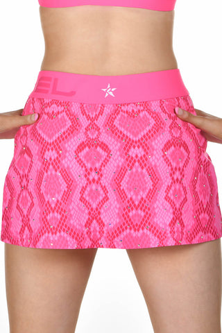 A close-up of a model wearing a bright pink athletic skirt with a snakeskin pattern and rhinestone embellishments, featuring a pink waistband with a white star logo.