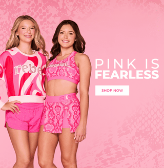 A pink promotional banner featuring a model wearing a pink lounge set and workout set against a bright pink background, with large text reading 'PINK IS FEARLESS' and a 'SHOP NOW' button.