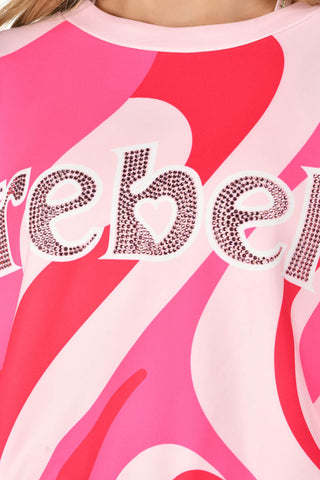 Close-up of a pink and white abstract graphic sweatshirt featuring a rhinestone-embellished 'Rebel' text across the chest.