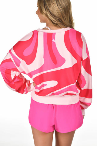 A woman shown from the back wearing a vibrant pink and white abstract patterned sweatshirt and matching hot pink shorts against a plain white background.
