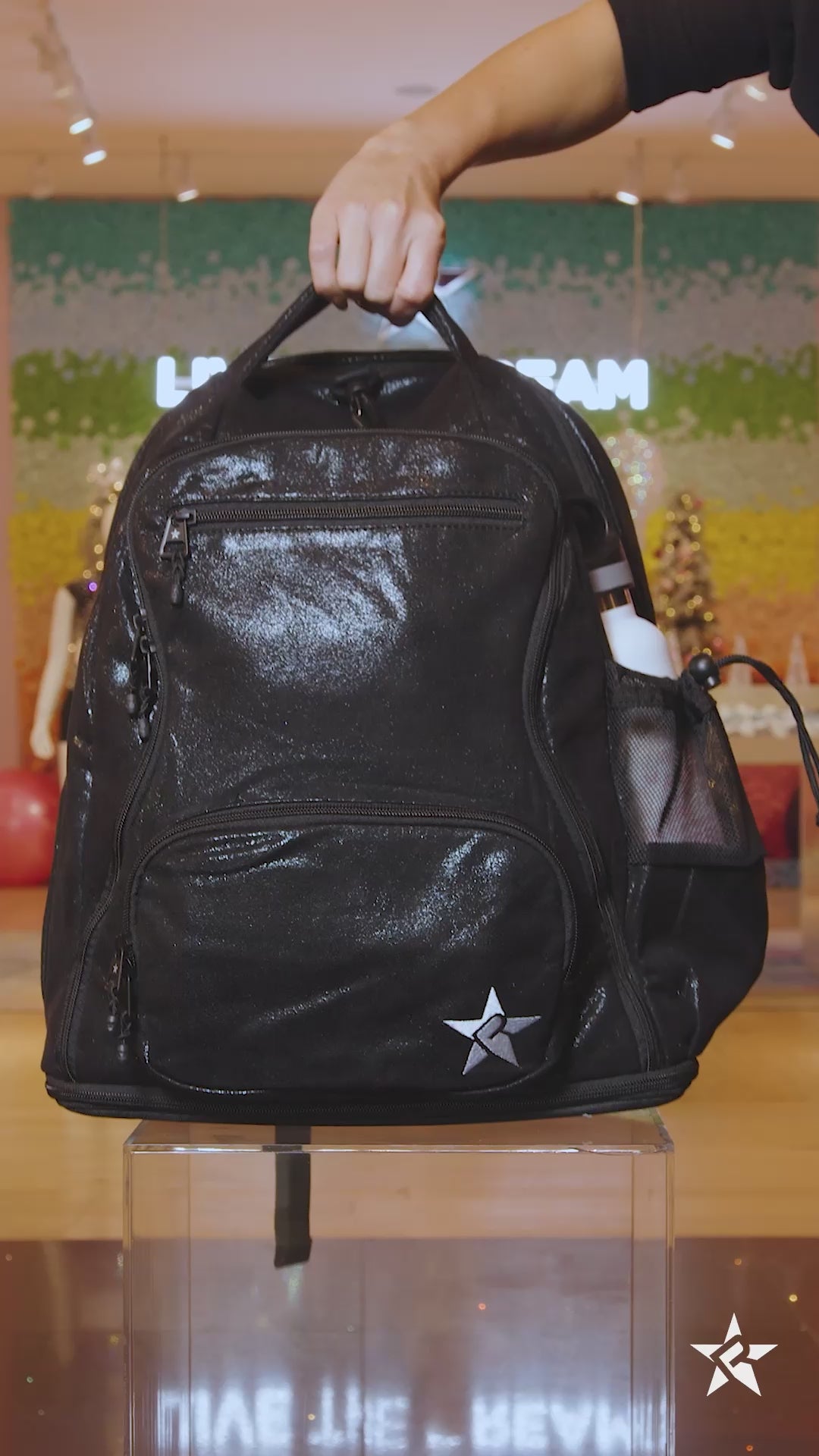 A 15-second video showcasing a black glittery Dream backpack, highlighting its multiple compartments and storage capacity. The video demonstrates various items that can be stored inside, including shoes in the bottom section. 
